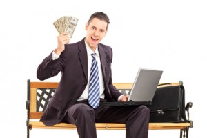 Happy businessman with laptop sitting on a wooden bench and holding US dollars isolated on white background